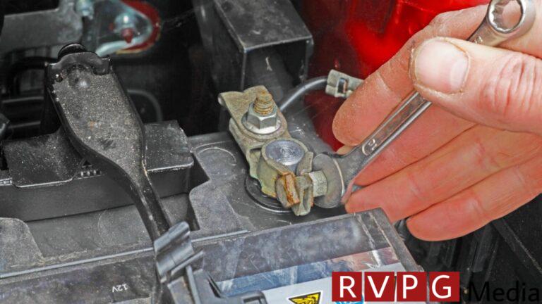 A person using a wrench to disconnect a car battery.