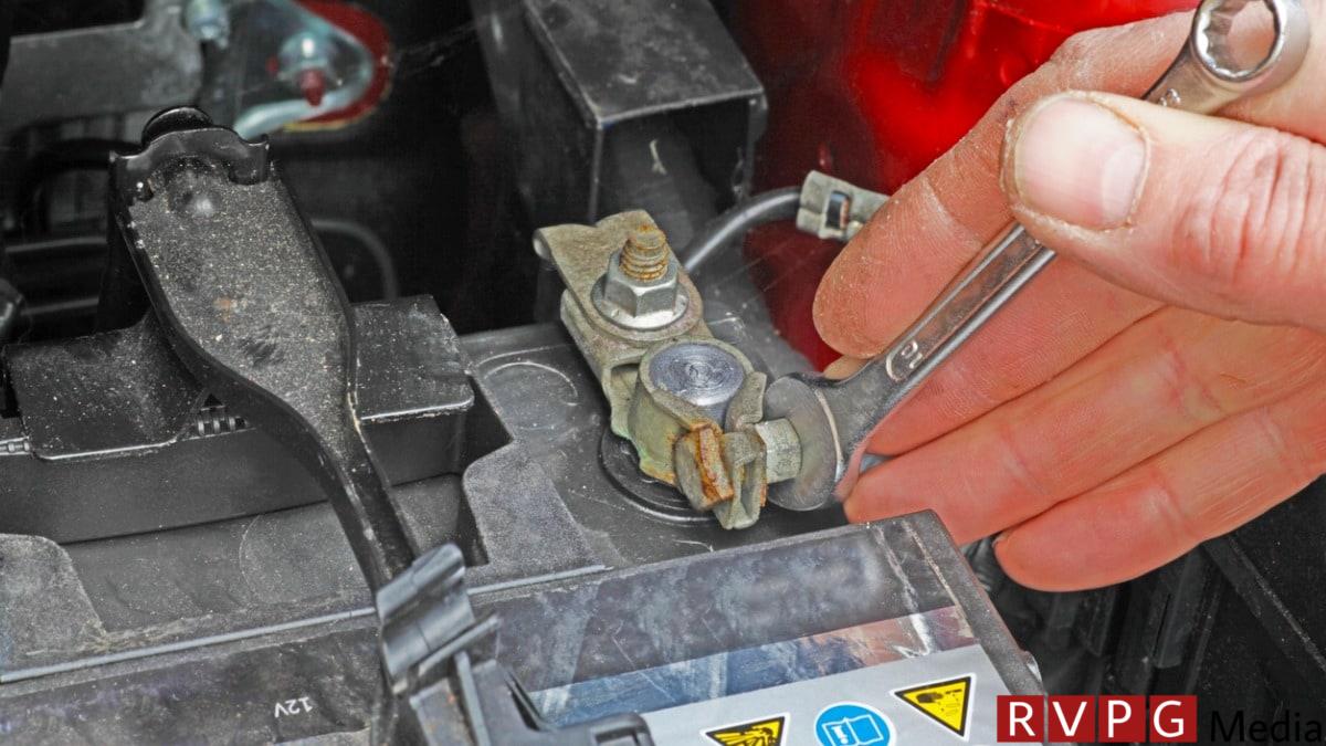 A person using a wrench to disconnect a car battery.