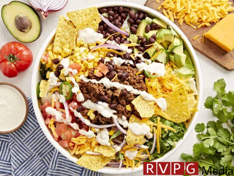 overhead view of taco salad with creamy white dressing and corn chips in a white bowl.