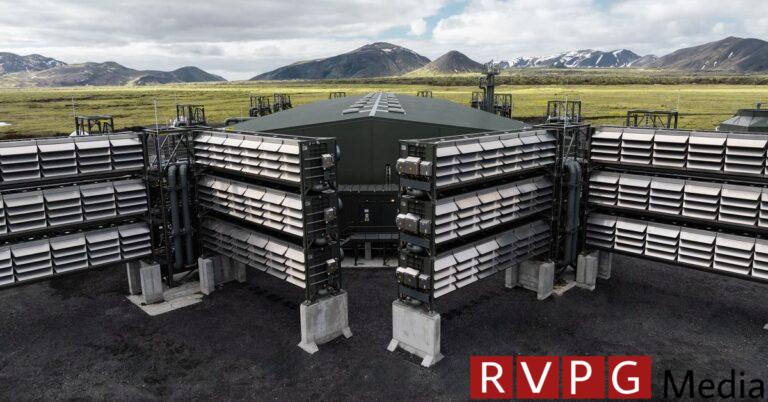 Large equipment that looks like stacked containers with slots running across it. A grassy valley and mountain range can be seen behind the equipment.